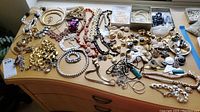 Full assortment of costume jewelry spread out on wooden surface, showing bracelets, necklaces, pins, earrings.