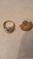 Top-down image of the gold ring with curved design and circular pin inscribed Group President with emblem.