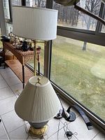 Brass floor lamp and table lamp beside window on a table next to two black desk lamps on floor