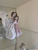 Side view of Lladro mother and child figurine on a glass shelf.