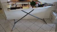 White ironing board with metal legs holding various office supplies and household items.