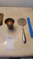Photo showing the small sterling silver cup and serving utensil side by side on a beige surface.