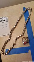Photo showing full necklace and heart pendant arrangement on surface with lot tag.