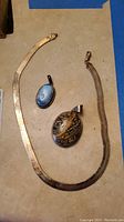 Top view of the herringbone necklace laid with the two pendants, showing the length and style of the necklace and the oval shape of the pendants