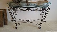 Front view of the table showing scalloped glass top and ornate metal base with scroll and floral detailing.