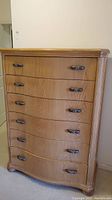 Frontal view of the tall wooden dresser showing five curved drawers with two metal handles on each drawer.