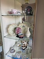 Glass cabinet with multiple shelves holding various teacups, saucers, decorative plates, and vases.