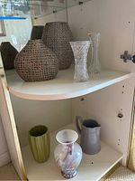 Shelf display of seven decorative vases including ceramic, glass, and pitcher style