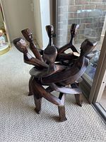 Full view of the wood sculpture showing five human figures holding hands in a seated circular arrangement.