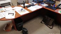 L-shaped office desk with papers and office supplies visible on top, showing laminate surface with scratches.