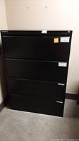 Front view of black metal file cabinet showing four drawers with some minor scratches