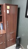 View of the filing cabinet closed showing the locking door on top and two filing drawers below, brown laminate finish, cabinet beside a wall and a framed picture.