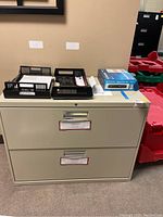 Front view of cream lateral filing cabinet with two drawers and various office items on top.