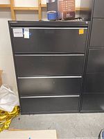 Front view of black 4-drawer filing cabinet with keys attached to top drawer lock, displaying cabinet height and drawer configuration.