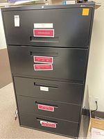 Front view of the black lateral filing cabinet showing the 5 compartments with various size drawers and lock on top drawer.