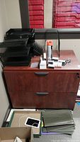 Front view of wood lateral filing cabinet with metal drawers, keys, and office supplies on top. Shows surface scratches.