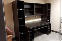 Full view of the dark covered particleboard office cabinet with upper shelving, side shelving units, desk surface, and wine rack cubbies underneath.