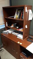 Front and side view of the office cabinet showing two shelving levels above and two drawers below with locks and handles. Various office items on shelves not included.