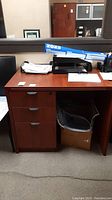 Front view of brown covered particleboard office cabinet with three drawers and scratches. Items on surface not included.