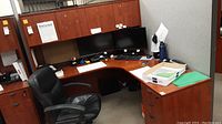 L-shaped office desk showing desktop surface with two monitors and workspace, desk has visible scratches and wear marks.