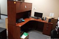 L-shaped office desk with attached hutch, drawers, and cabinet doors shown from the front and side, some office equipment placed on top.