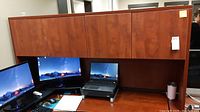 Full view of the office desk hutch on top of a desk with computer monitors and accessories below. Shows size and wood finish with some scratches.