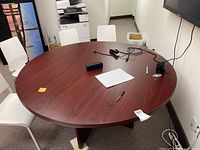 Top view of brown round conference table with various office items on it, showing surface scratches.