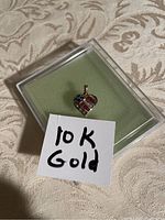 Photo of the 10K gold heart-shaped charm with American flag design, placed in a clear case with a handwritten 10K Gold note.
