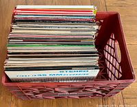 Top angle view of a red plastic crate filled with approximately 60 vinyl records showing assorted album covers and edges.