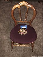 Front view of the antique wooden chair showing the spindle backrest and floral needlepoint upholstered seat.