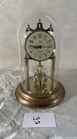 Front view of the anniversary mantel clock under a glass dome showing the clock face and brass pendulum