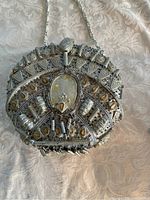 Front view of vintage metal pocketbook purse showing ornate embossed metal decoration and decorative clasp with chain strap.