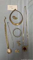 All gold jewelry items arranged on a blue cloth background including necklaces, bracelets, rings, earrings, brooch, and cufflinks.