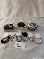 Photo shows three decorative ladies powder containers and six assorted bracelets laid out on a patterned fabric background for viewing.