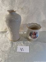 Tall white embossed floral pattern vase with gold rim and smaller scalloped rim vase with angelic image, both shown side by side on white background.