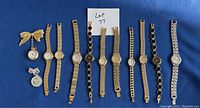 Photo showing 10 ladies wristwatches with various gold and silver-tone stretch and link bands, plus 2 decorative watch pins (a bow pin with dangling watch and ornate pin).