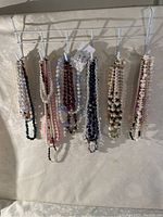 Seven beaded necklaces hanging on a rack, showing various bead colors and styles.