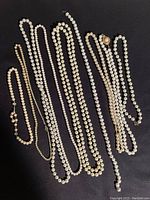 Seven pearl necklaces arranged side by side on a dark surface to display variation in length, bead size, and clasp design.
