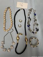 Assorted jewelry pieces including necklaces, earrings, and bracelet arranged on light grey fabric background with lot number card.