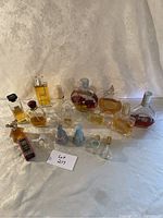 Front view of assortment of 15 perfume bottles and powder container on cream fabric background