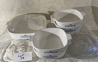 Photo showing white ceramic CorningWare baking dishes with Cornflower Blue pattern with clear glass lids arranged on a flat surface