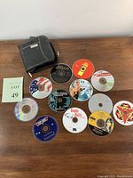 Top view of all 12 CDs and black carrying case laid out on wooden surface showing disc artwork and case size.