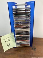 Stack of 23 music CDs and blue CD holder seen from front angle with lot label