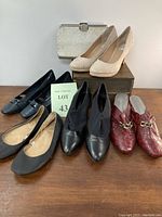 Five pairs of size 8 women’s shoes and a silver textured evening clutch bag arranged on and in front of a wooden box against a white background.