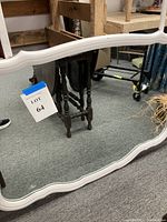 Close-up photo of large white dresser mirror showing the white curved frame and part of metal arm for hanging.