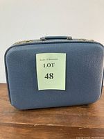 Front view of vintage blue train case with 'Lot 48' label, showing textured surface and case shape.