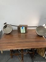 Full view of the vintage headlight bar with two headlights mounted at each end, placed on a wooden tabletop. Shows rust on one headlight casing.