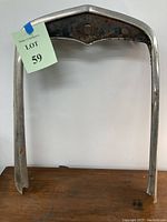 Front view of a single old antique car radiator casing standing upright on a brown surface against a white wall, with a lot label attached.