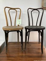 Photo of two bentwood chairs, one natural wood finish and one black, showing splayed legs and rounded backrests.
