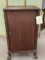 Full front view of the cabinet showing closed wooden door with carved detailing on vertical side columns and claw feet.
